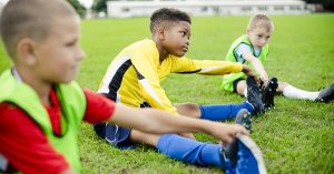 Diverse kids stretching on the field; blog: prevent fall sports injuries