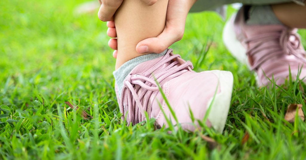 Female teenager hand touching painful twisted or ankle sprain,feel ache,ankle injury after exercise at park,asian child girl have leg pain or broken ankle,problem,accident while running,playing on the lawn; blog: 9 Most Common Sports Injuries in Children