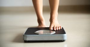 Female leg stepping on weigh scales. Healthy lifestyle, food and sport concept; blog: A Guide to Weight Loss and Joint Replacement Surgery