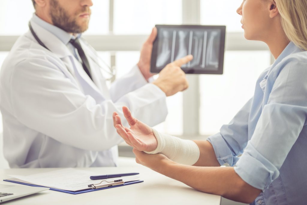Cropped image of handsome medical doctor talking to female patient with damaged hand and showing her an X-ray picture on tablet while working in his office; blog: When to See an Orthopedic Doctor